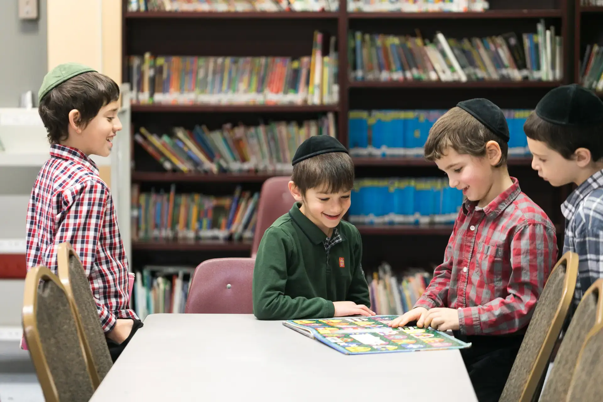 Young Jewish boys wearing kippot happily read a colorful book in a Milwaukee Jewish school library.