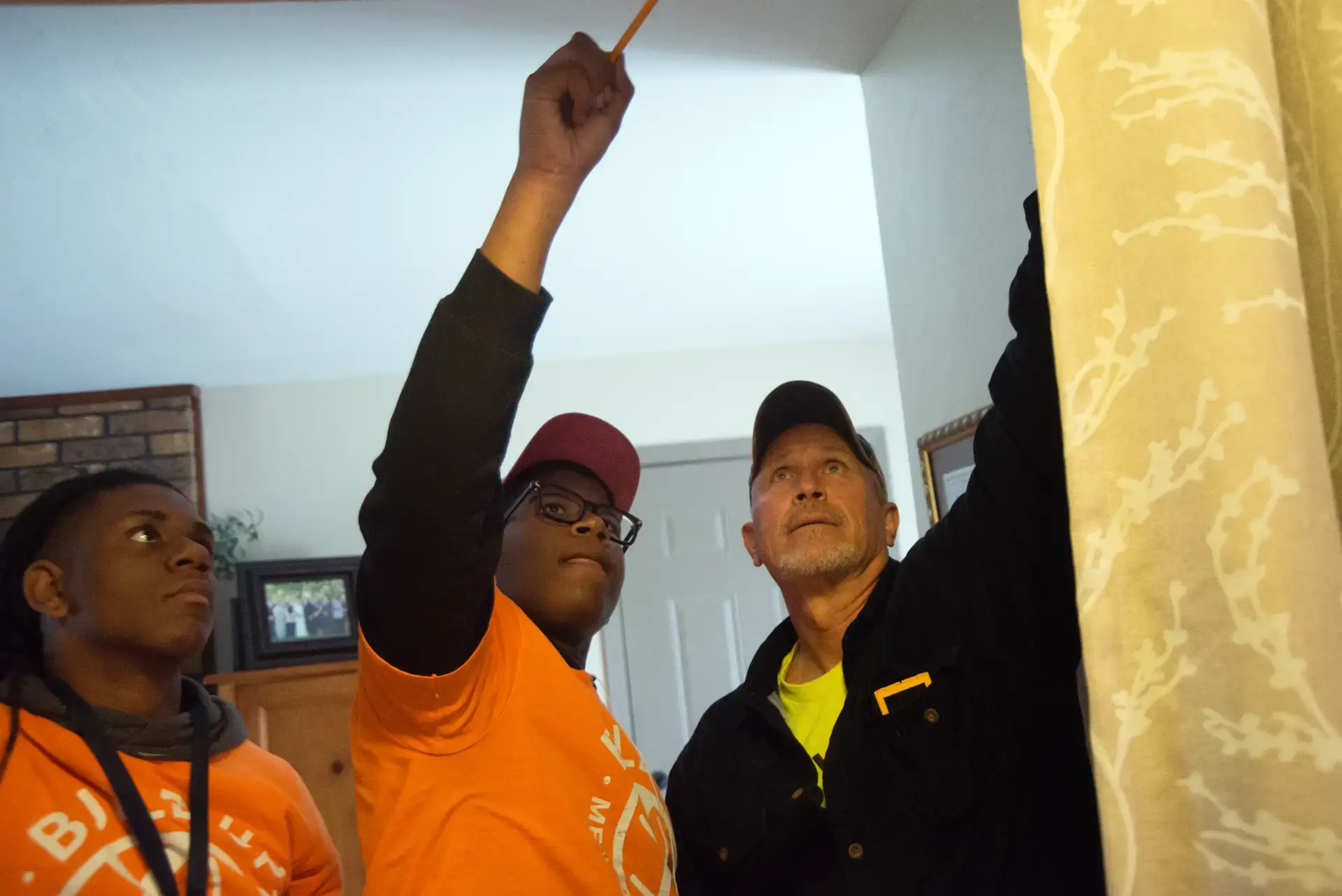 Young people learning practical skills, measuring ceiling with mentor during youth development program.