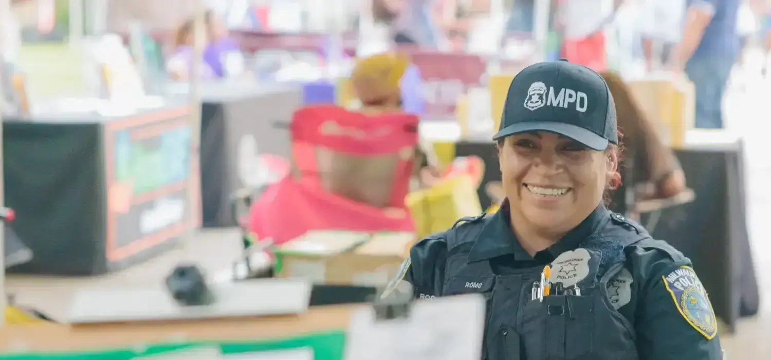 Smiling female Milwaukee Police Officer Romo in uniform and MPD cap, engaging with the community at an outdoor event.