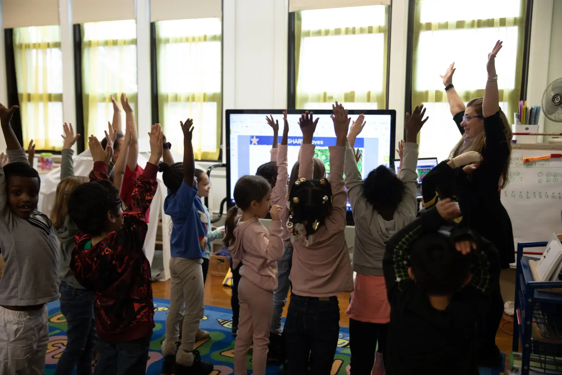 Diverse students raise hands in an urban classroom, engaging with a teacher during a SHARP Literacy program lesson.