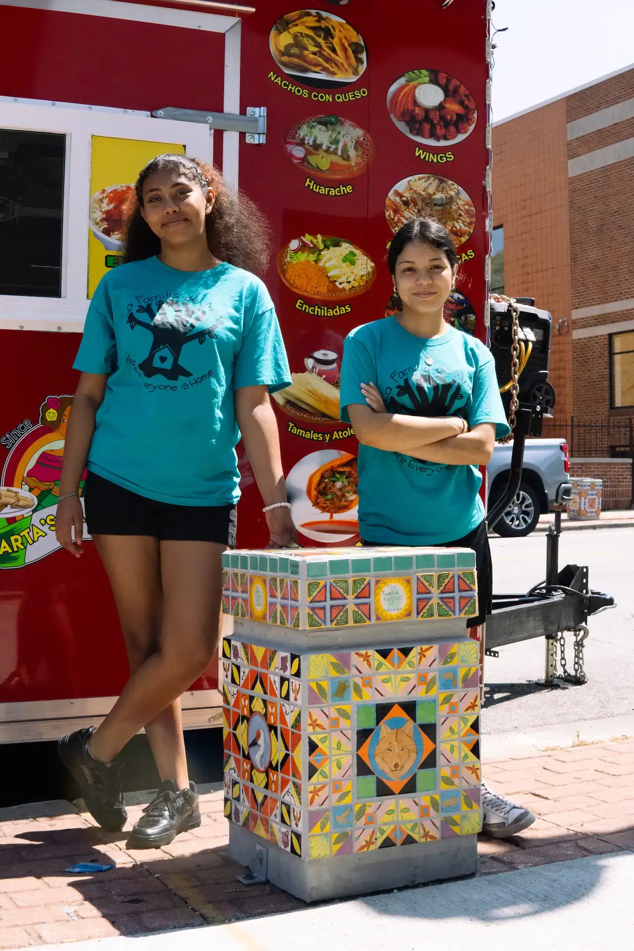 La Familia De Arte youth program participants pose by a Mexican food truck and an artistic tiled pillar, 2023.