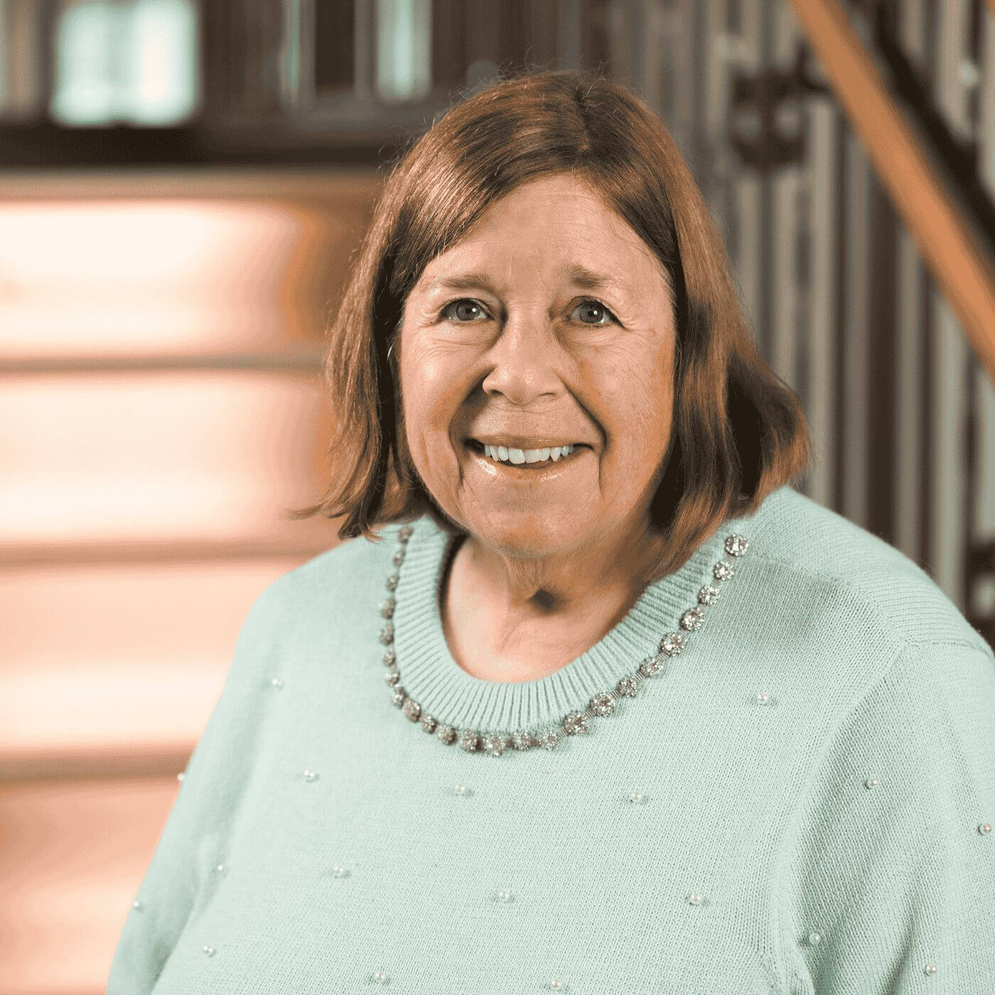 Close-up portrait of Helen, a smiling senior woman with short brown hair, wearing a mint green embellished sweater.