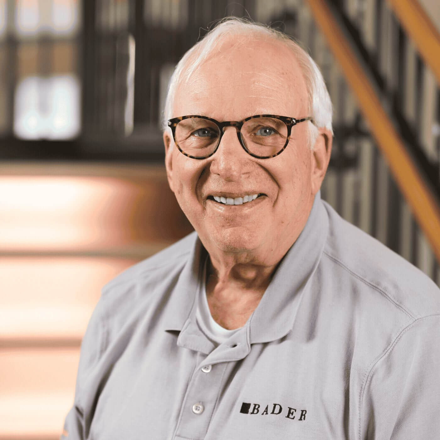 Professional portrait of Jeff Bader, a smiling man with white hair, wearing glasses and a grey BADER polo shirt.