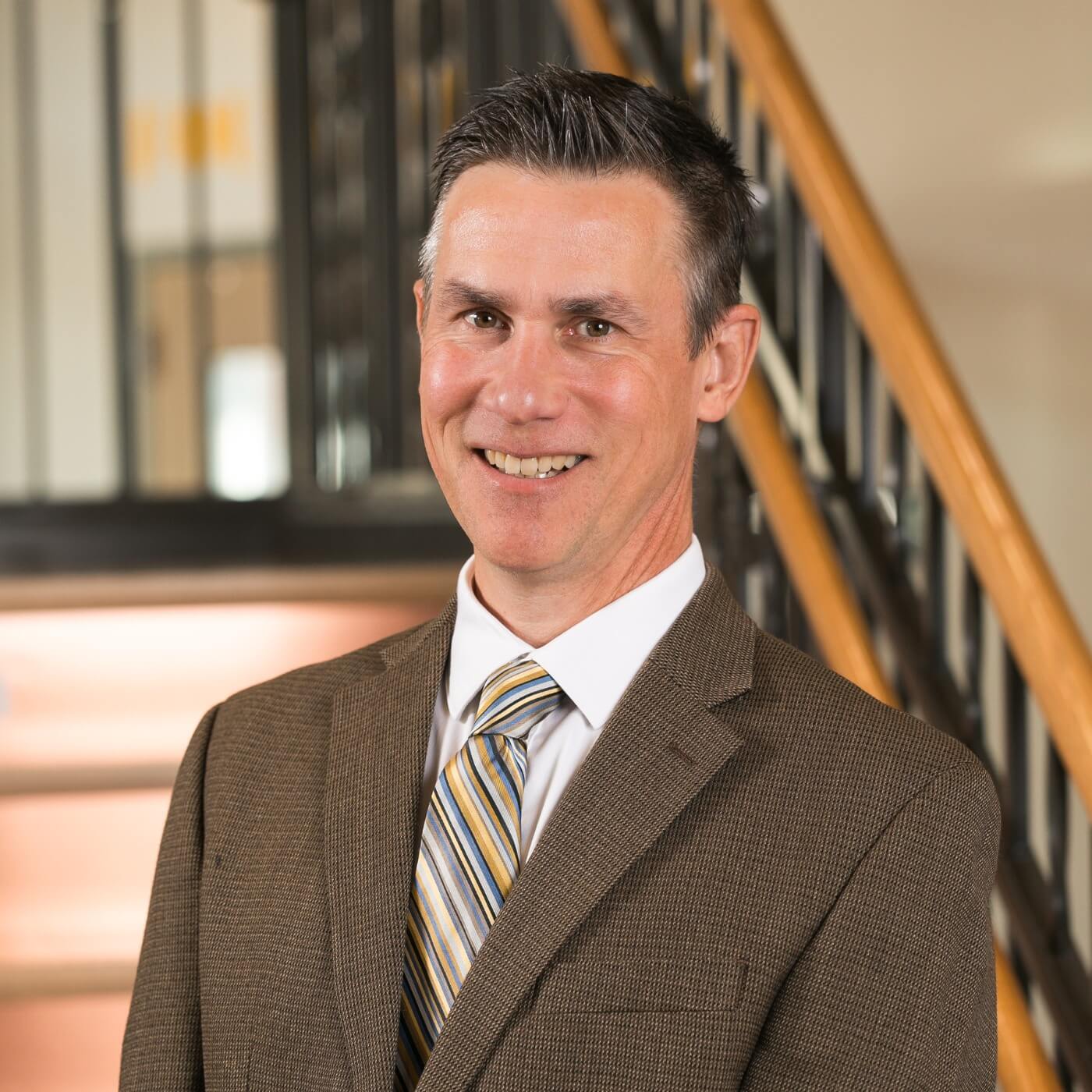 Robert, a smiling professional man in a brown suit and striped tie, standing in a modern office.
