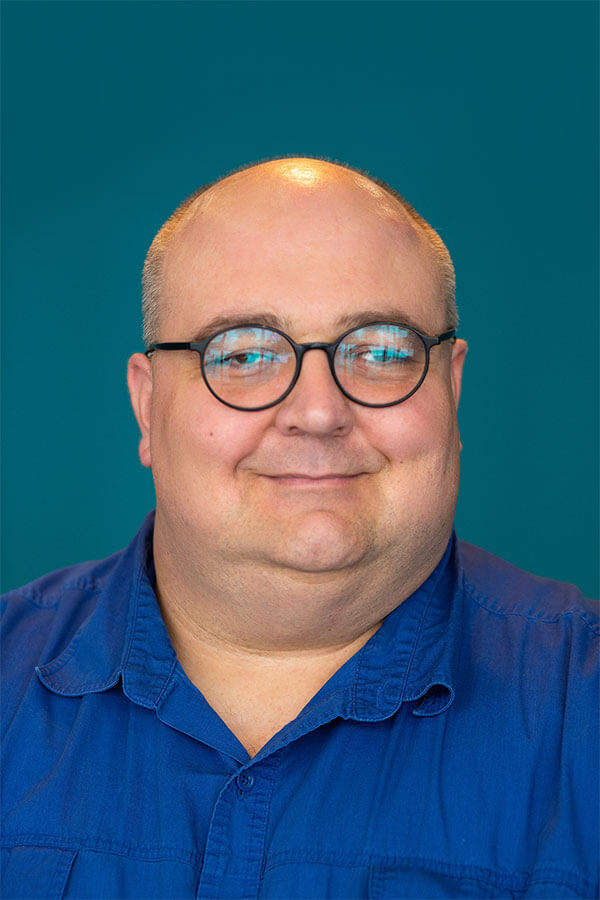 Brian Repinski, bald man with glasses and a friendly smile, wearing a blue shirt against a teal background.