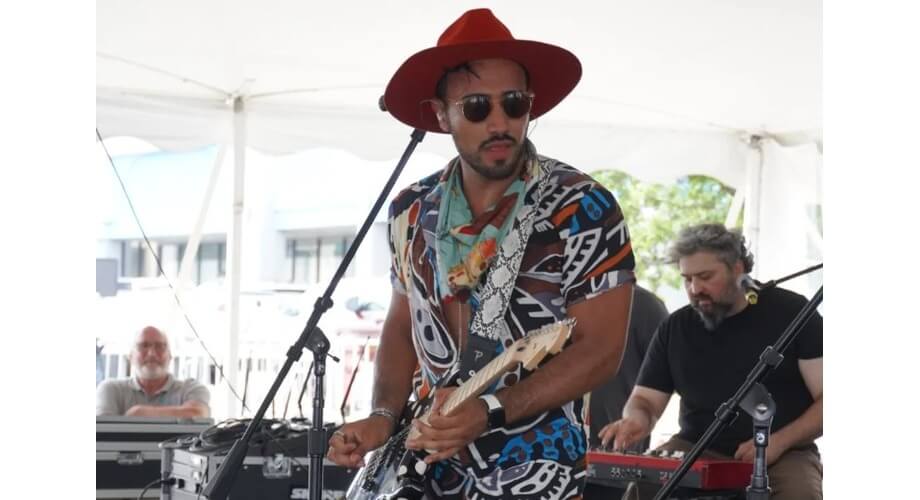 Guitarist in red hat performing live with band Musician in red fedora, sunglasses, and patterned shirt plays electric guitar with band at outdoor concert.