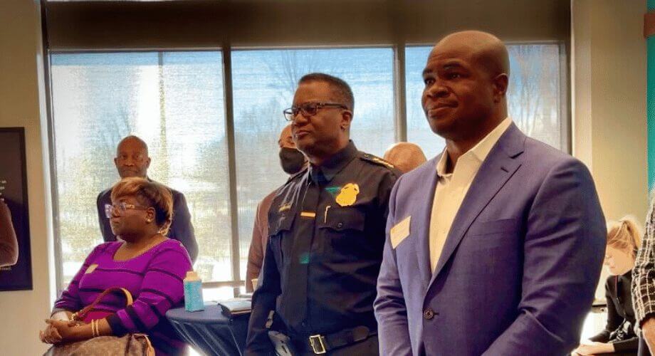 Black leaders, including a man in a blue suit and a police officer, attend a community recognition event.
