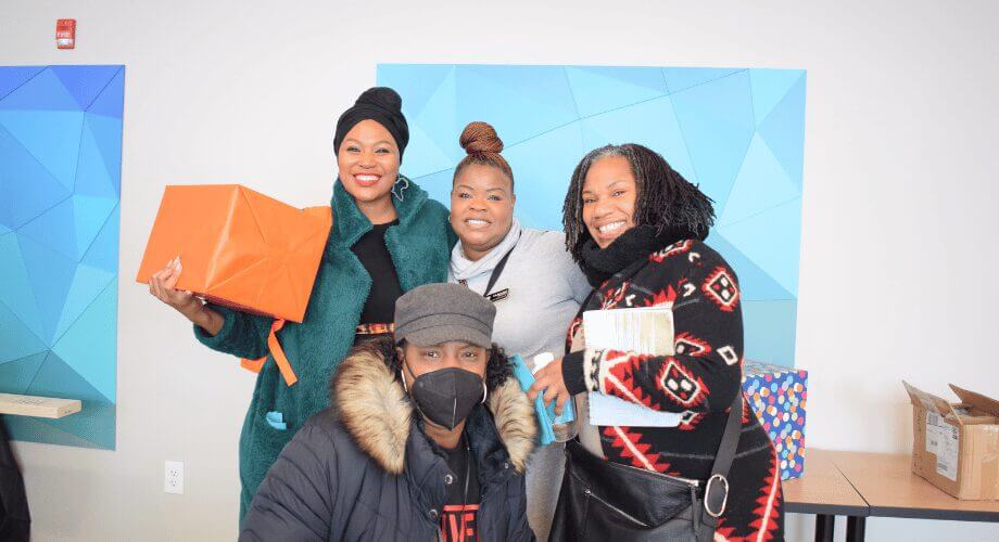 Four diverse women smiling with gifts and packages at a joyful community event with Bader.