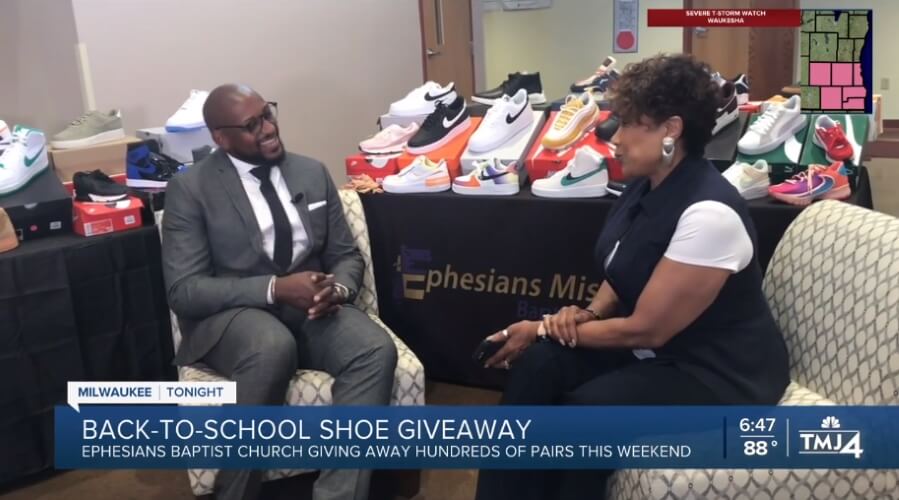 Two people interviewed about Ephesians Baptist Church's Milwaukee back-to-school shoe giveaway. Display of sneakers.