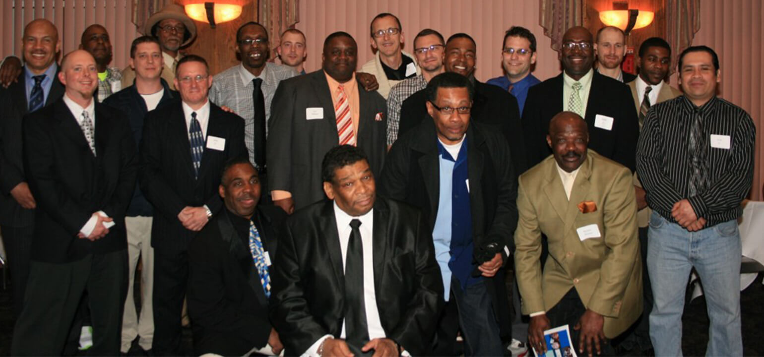Diverse group of professional men in suits and ties smiling at a Legacy Serenity Inn gathering or conference.
