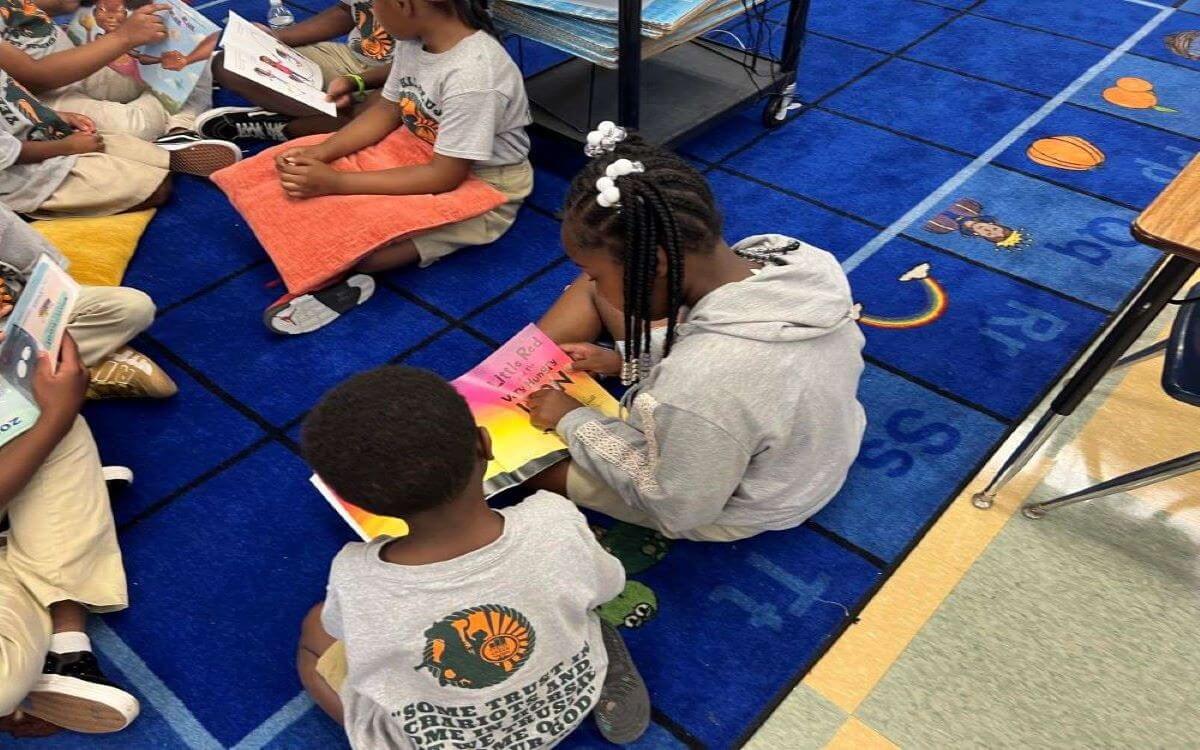 Diverse elementary students sit on a blue alphabet rug, engrossed in reading books during classroom story time.