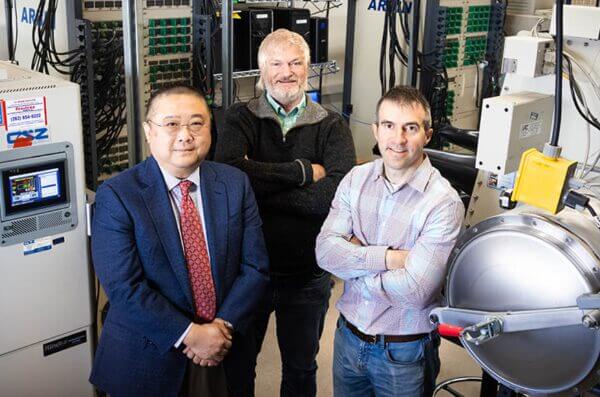 Three scientists and engineers in a high-tech research lab. One in suit, one bearded, one by environmental test equipment.