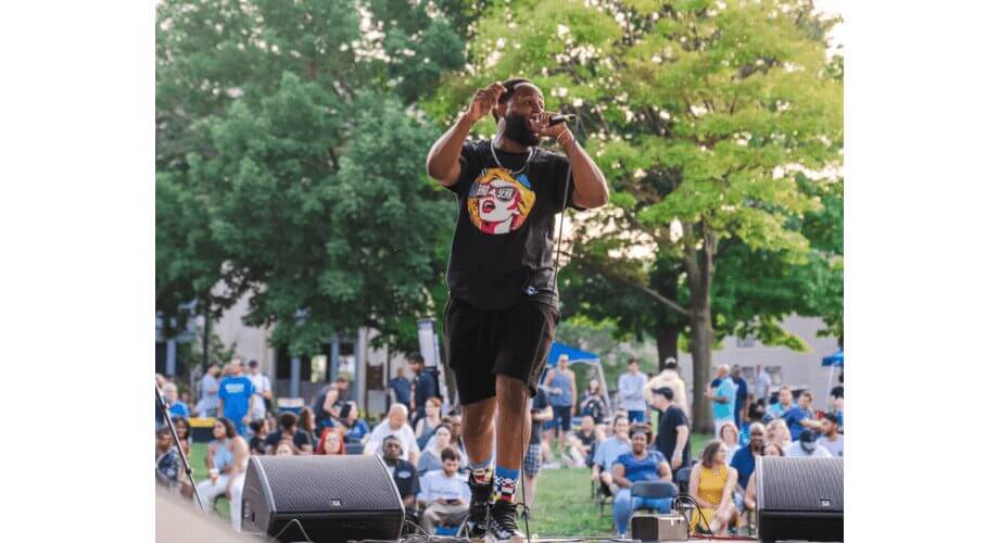 Rapper Performing Live at Outdoor Music Festival Energetic male artist singing live on an outdoor stage, engaging the audience at a summer music event.
