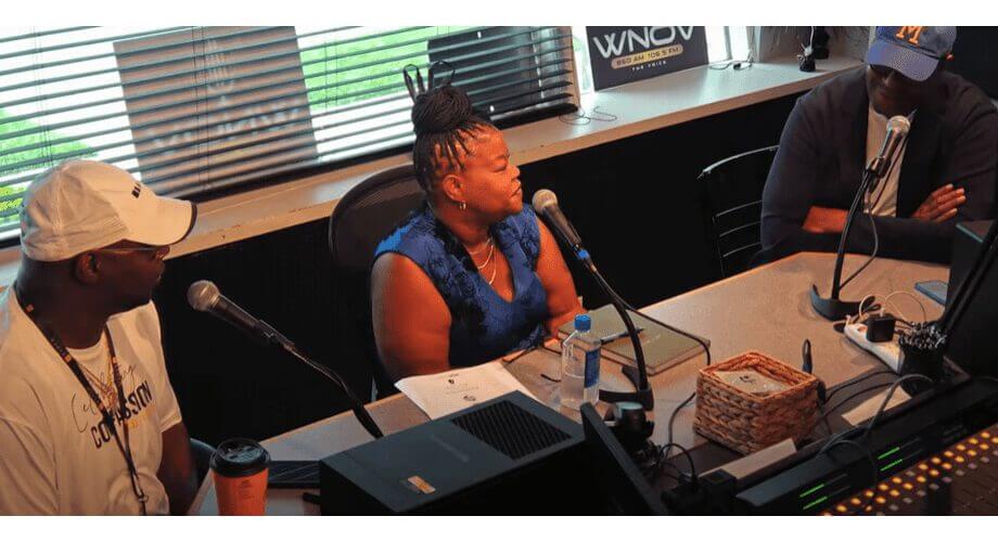 Three people, including a woman in blue, participate in a WNOV radio interview in a broadcast studio with microphones.