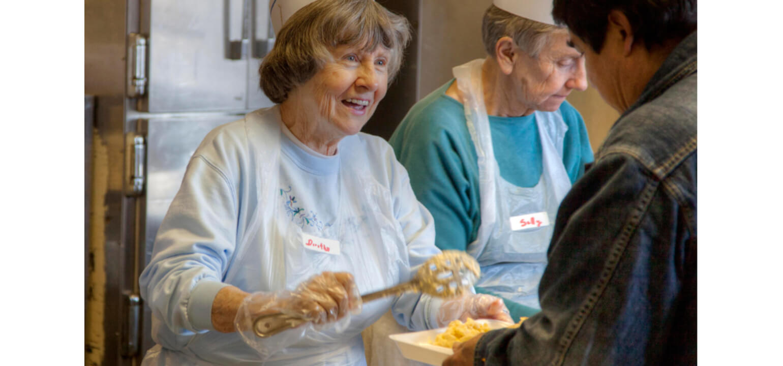 Smiling Bertha and Sally serve a warm community meal at The Gatherings of SE-WI event to a happy guest.