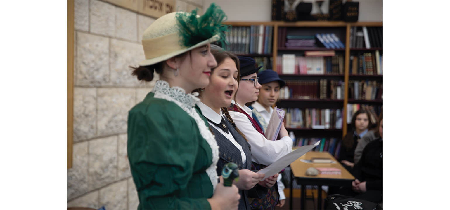 Torah school girls in period costumes sing from sheet music during a historical play or performance.