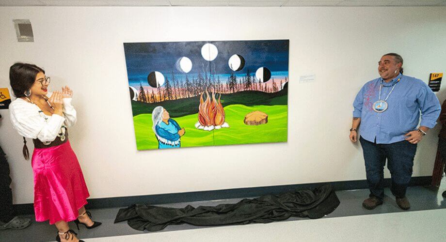 UWM: Indigenous Sovereignty Murals Unveiled UWM event: Indigenous woman applauds new mural unveiling. Artwork features a bonfire, moon phases, and traditional figure, celebrating sovereignty.