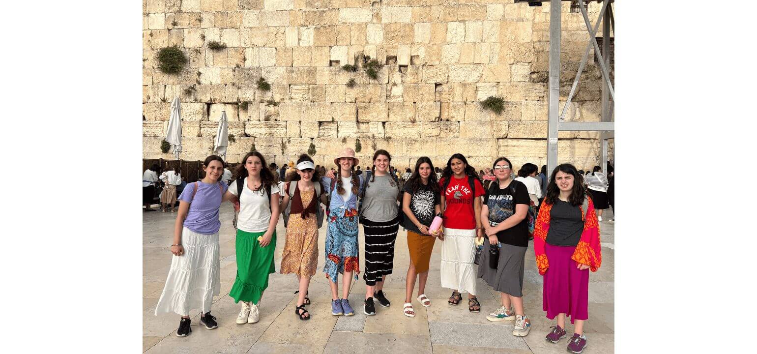 Smiling group of young women visiting the ancient Western Wall (Kotel) in Jerusalem, a significant Jewish heritage site.