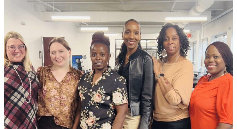 Six smiling professional women from diverse backgrounds posing together in an office. Represents teamwork and inclusion.