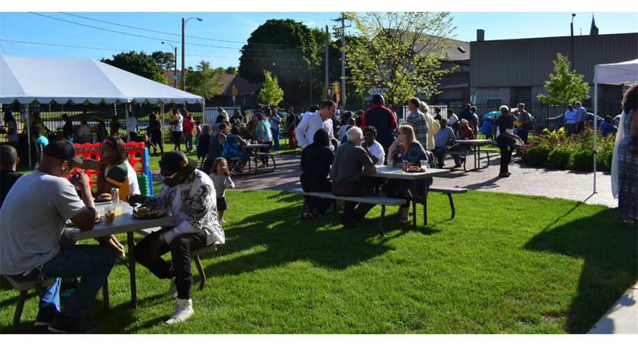 Community members enjoy food at picnic tables on a sunny day during the Bader BBQ outdoor gathering.