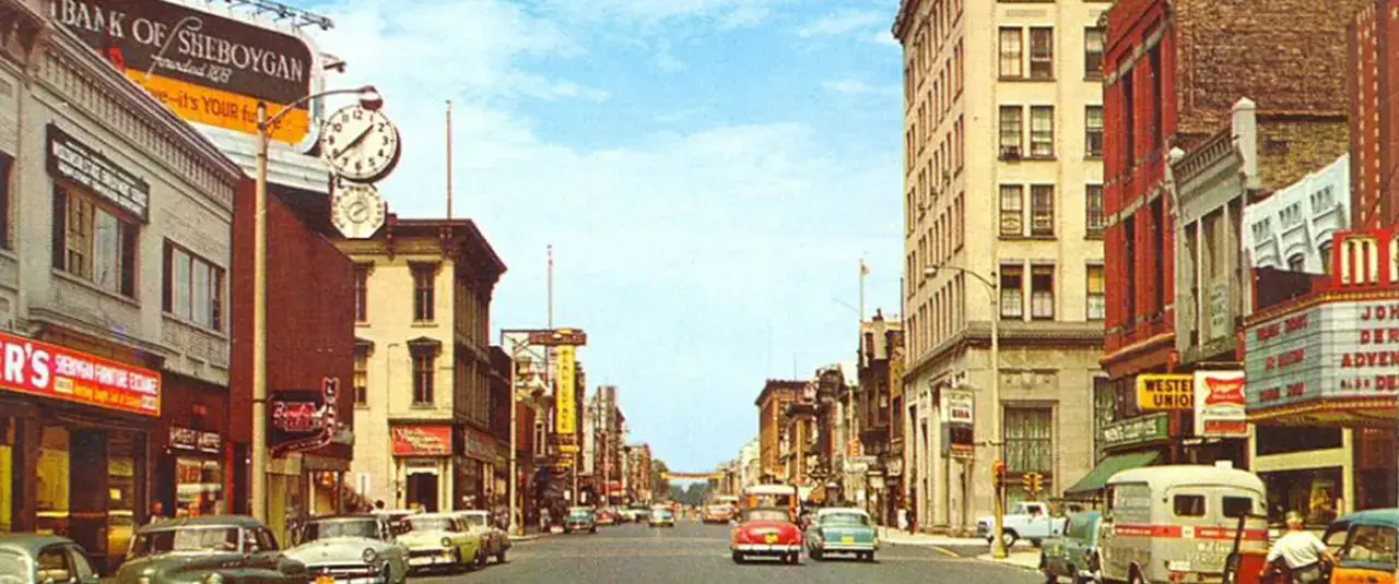 Did You Know? Bustling 1960s Sheboygan downtown. Bank of Sheboygan, classic cars, movie theater, street clock visible.