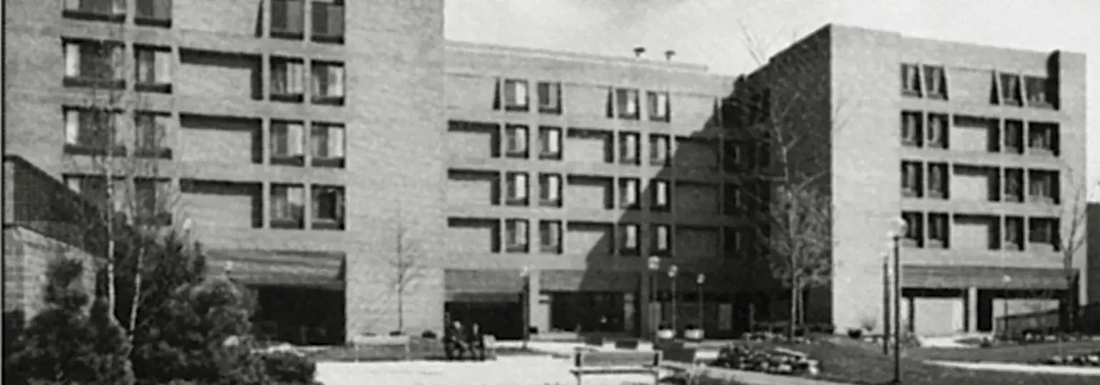 Vintage black and white photo of a large brick building with striking 'L' pattern windows and landscaped grounds.