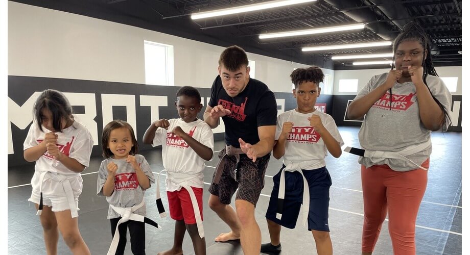 City Champs Youth Martial Arts & Self-Defense Training Instructor teaching diverse kids martial arts in a gym. Children in uniform practice self-defense stances at City Champs Foundation.