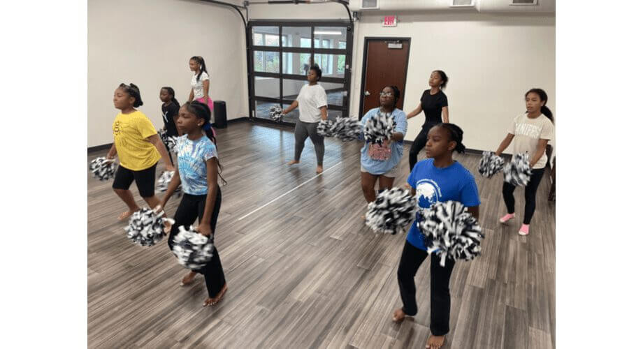 Diverse group of young girls practicing cheer and dance routines with black & white pom-poms in a studio.