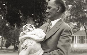 Vintage black and white photo of a man in a suit holding an infant in a blanket outdoors. Historical family portrait.