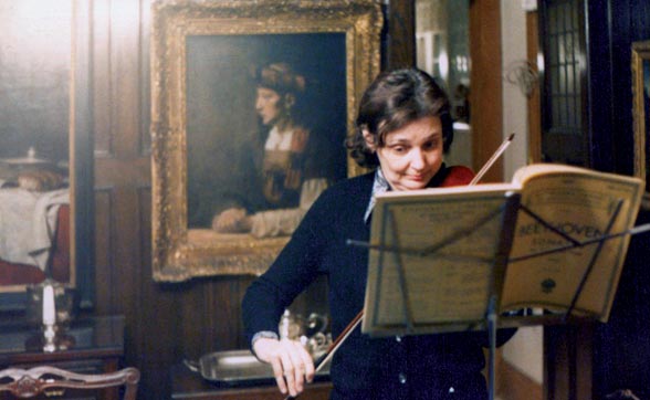 Helen Daniels Bader plays violin, reading Beethoven sheet music in a richly decorated room.