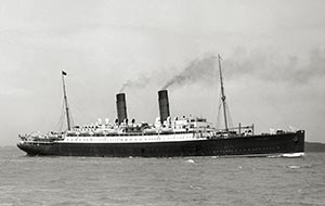Vintage black and white photograph of a large passenger ocean liner with two smoking funnels sailing on the water.