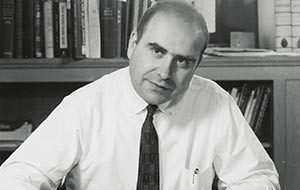Vintage black and white portrait of a serious man in a white shirt and tie, sitting in an office with books.