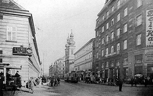 Bustling early 20th-century European city street with historic buildings, pedestrians, and vintage trams. iab-8
