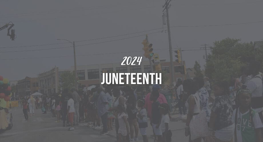 Crowd gathered on street for 2024 Juneteenth celebration, city buildings and traffic lights visible.