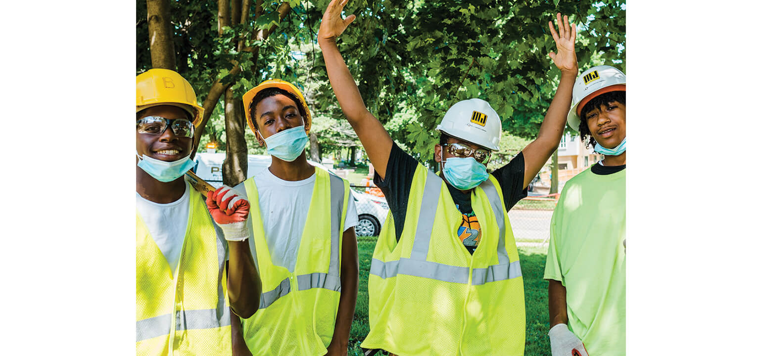Youth Kingdomworkers team smiling in hard hats, safety vests, and masks, enthusiastically ready for work outdoors.