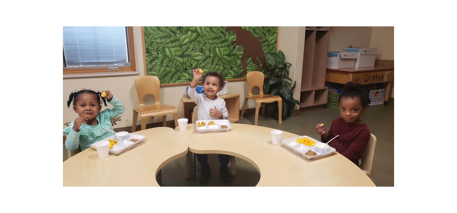 Diverse toddlers happily eat lunch at a crescent table in a Malaika ELC early learning center classroom.