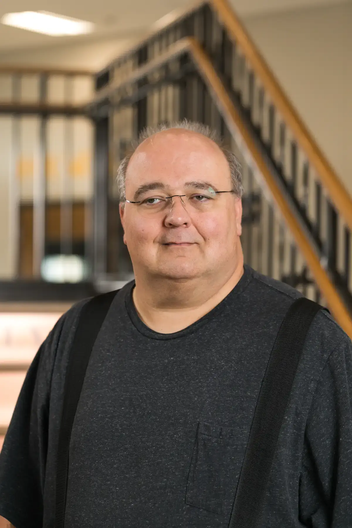 Brian Repinski professional business headshot. Smiling man with glasses in a grey shirt, blurred office background.