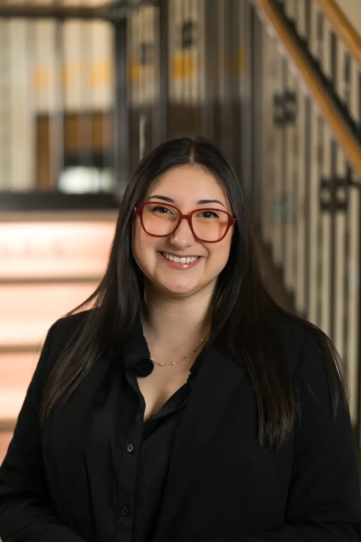Professional headshot of Claudia Martinez smiling, wearing red glasses and a black blazer.