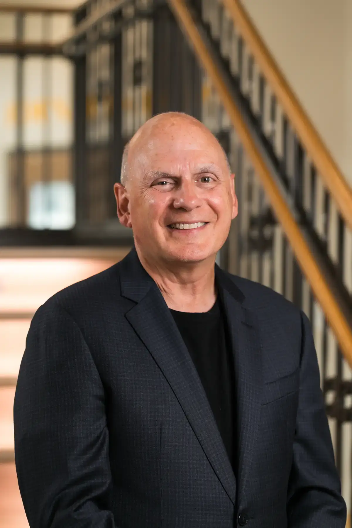 Professional headshot of Daniel J. Bader smiling, wearing a dark suit jacket, against a blurred office background.