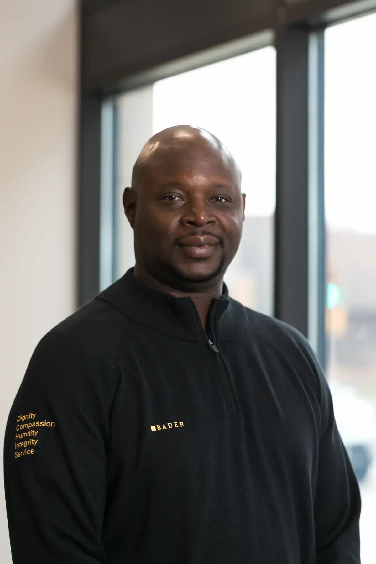 Professional headshot of Frank Harris, Jr., smiling, wearing a black Bader quarter-zip shirt with company values.