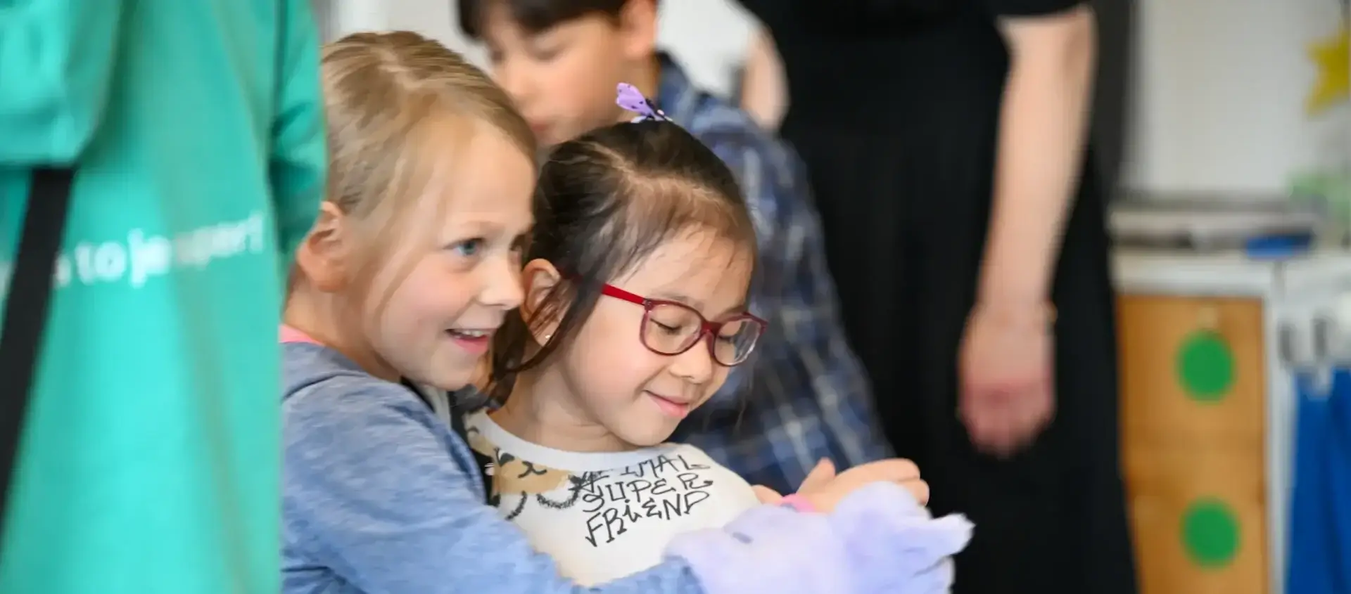 Smiling blonde girl embraces diverse friend with glasses, showing joyful friendship and community connection from grant programs.