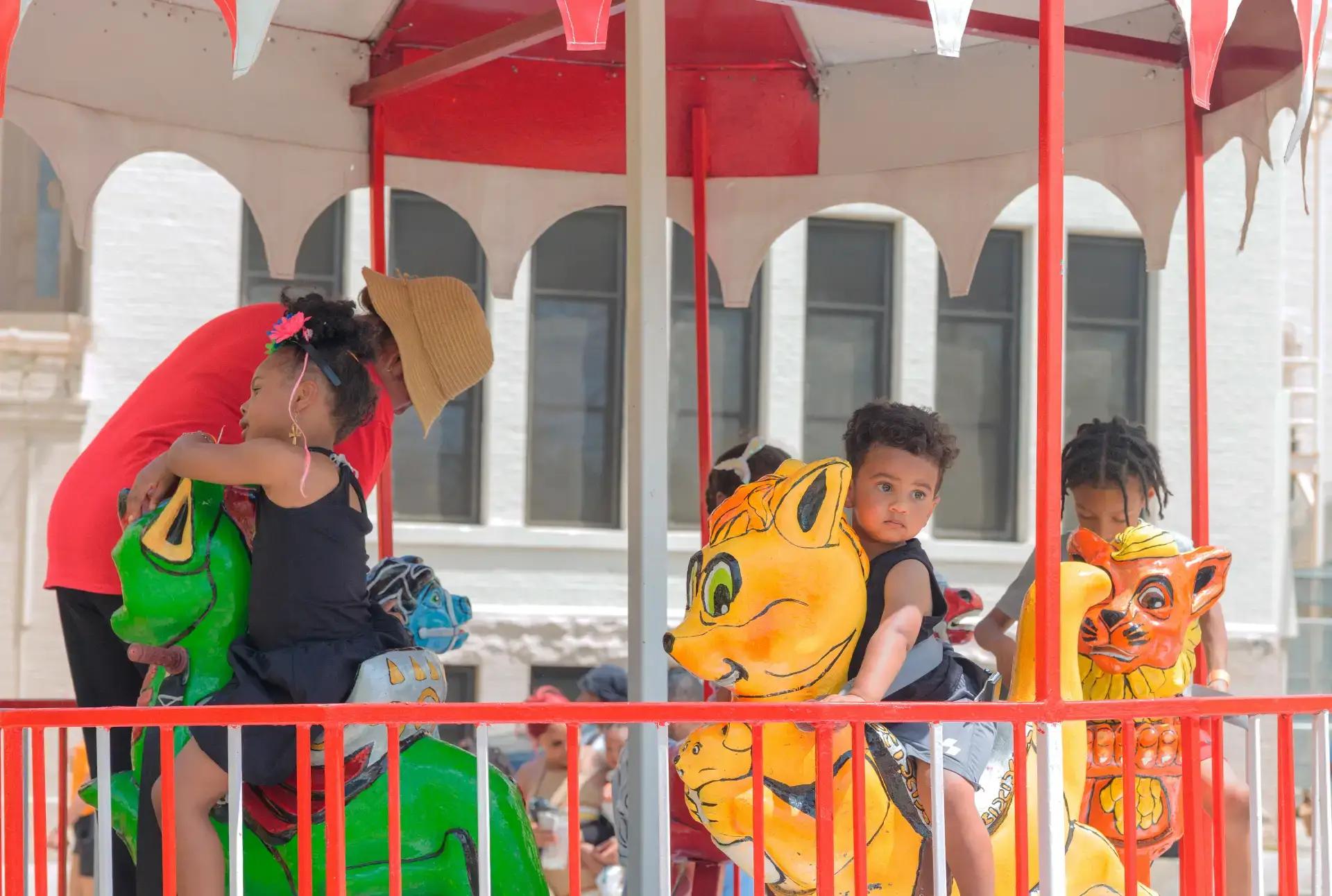 Joyful children riding a colorful carousel during a Juneteenth festival. A girl on a green animal, two boys on lion figures.