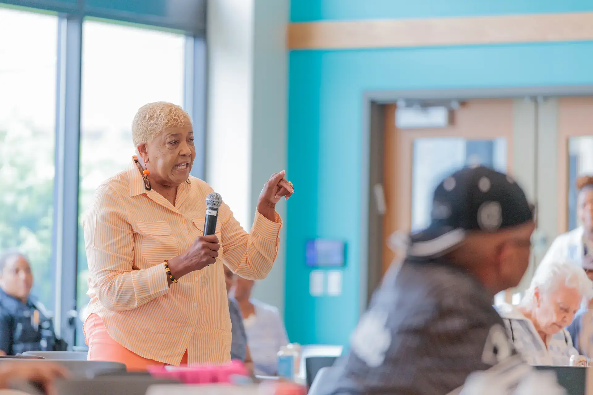 Senior speaker, Bader, passionately addresses community members with a microphone at a July 2025 neighborhood engagement event.