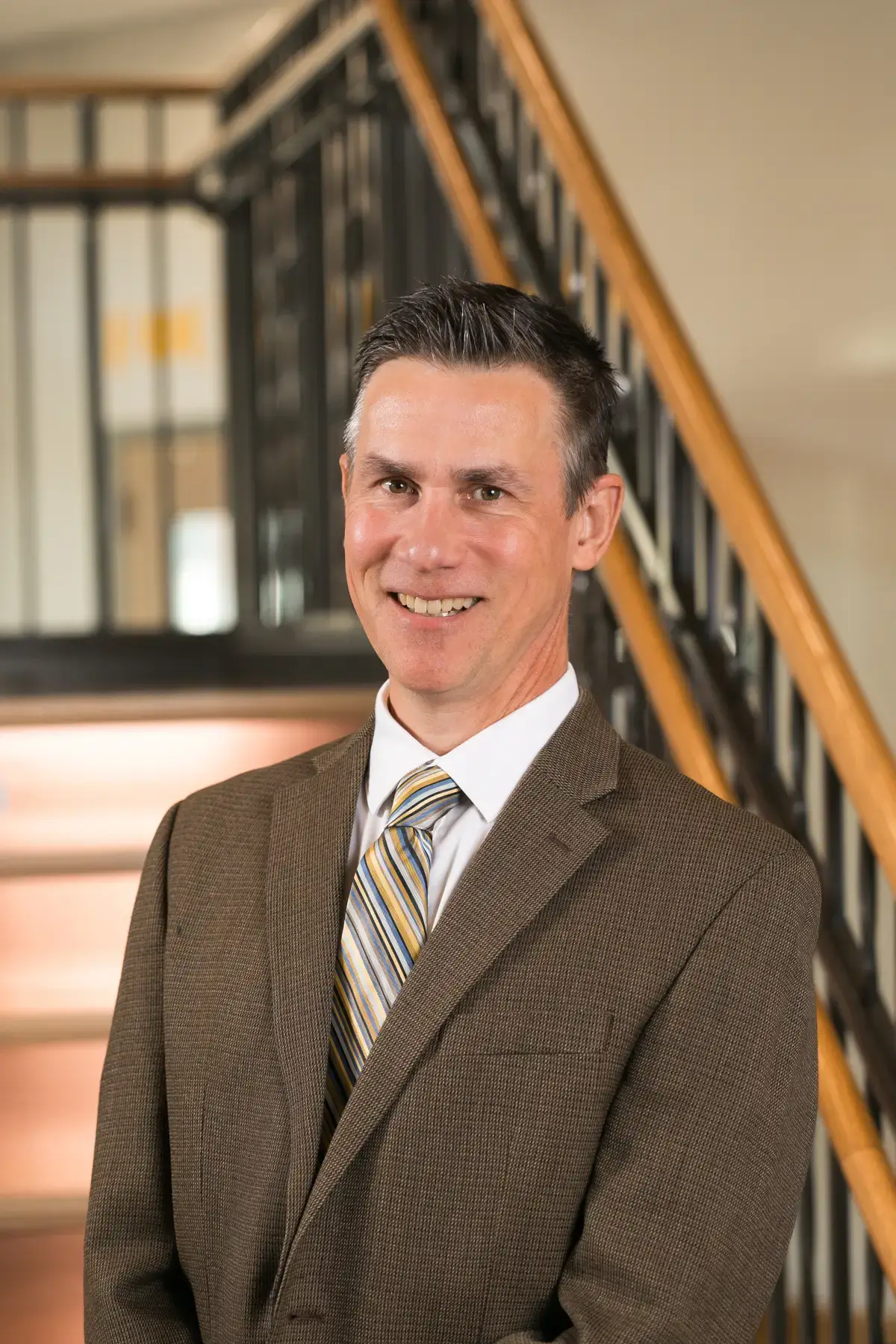 Professional headshot of Robert Tobon, smiling, wearing a brown suit and striped tie in an office setting.