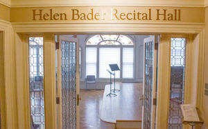 Entrance to Helen Bader Recital Hall, featuring open glass doors leading into a spacious, well-lit performance room with a music stand.