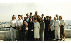 Diverse group of adults posing outdoors with a city view in 1999 for a historical timeline.