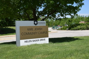 Karl Jewish Community Campus sign on Helen Bader Drive, featuring the Milwaukee Jewish Federation logo amidst green grass and trees.
