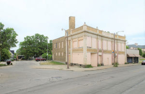 Historic urban corner building with boarded windows, tall chimney, and street, featured in a 2016 timeline.