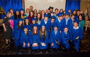 Graduates in blue caps & gowns with faculty & family celebrating their 2017 commencement. Confetti on the floor.