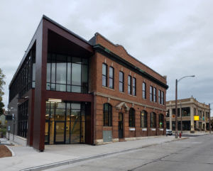 Exterior of a commercial building featuring historic brick and a modern dark-clad glass addition, likely from 2020 project timeline.